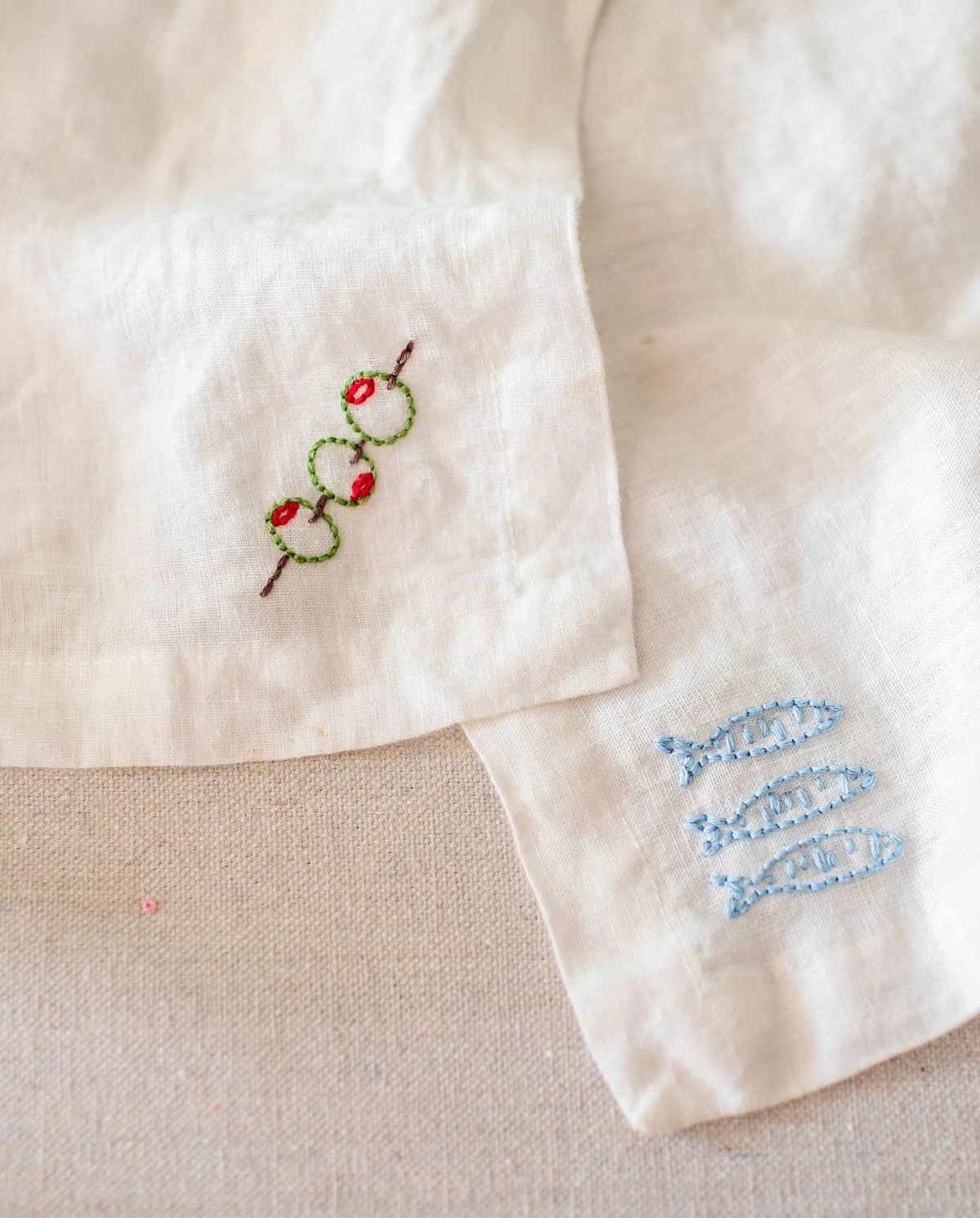Delicate embroidery on ivory linen featuring tiny green wreaths and pale blue fish